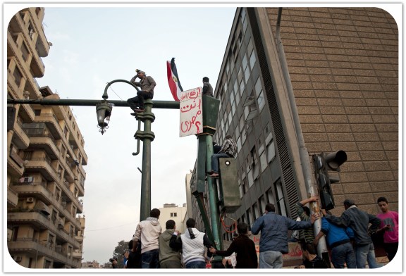 Youth watch nearby clashes atop a street lamp holding a sign that reads: "raise your head, you are Egyptian". November 2011. Photo: Ali Mustafa